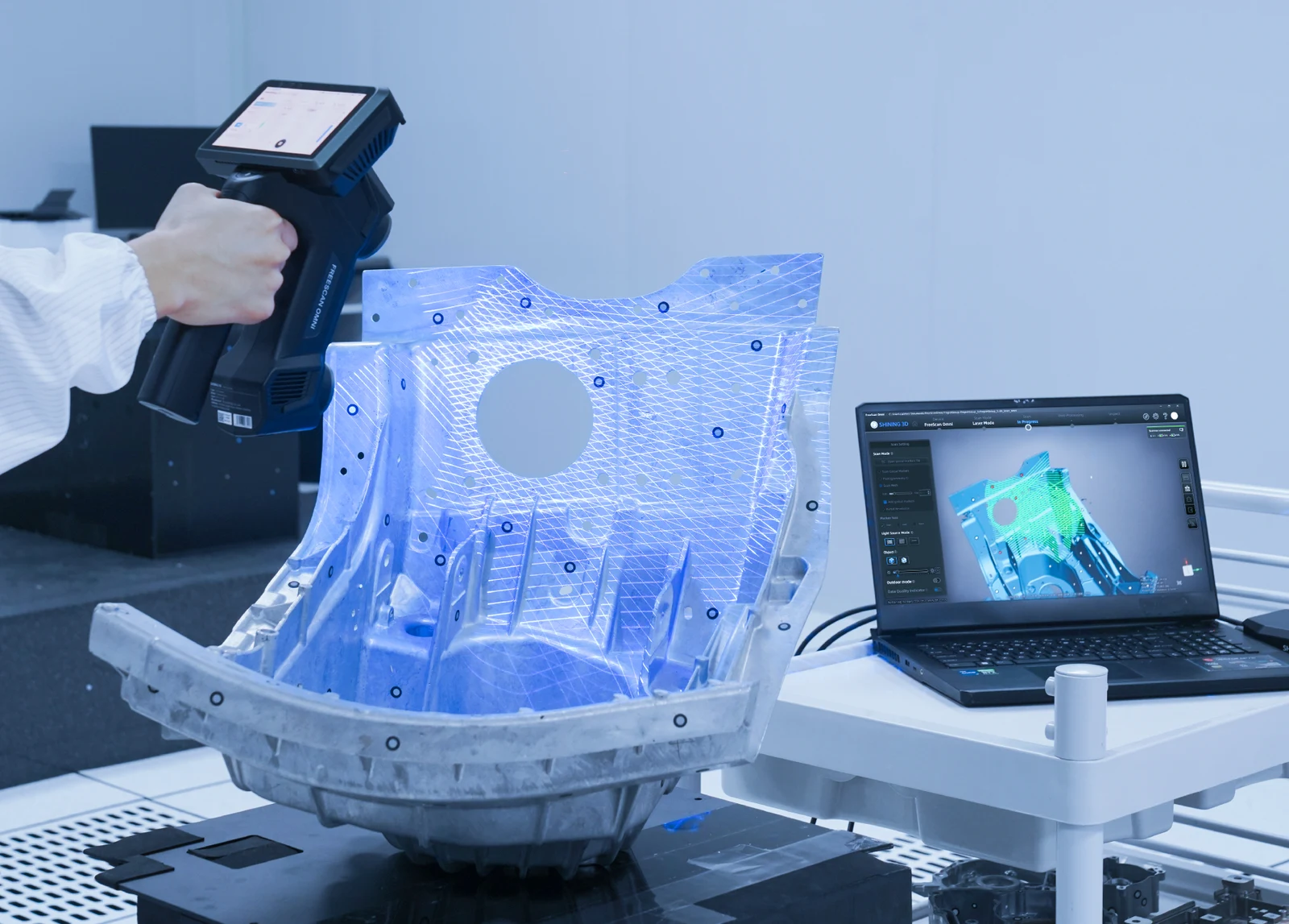 Scanner SHINING 3D FreeScan Omni en utilisation sur une pièce industrielle, avec projection laser bleu.
